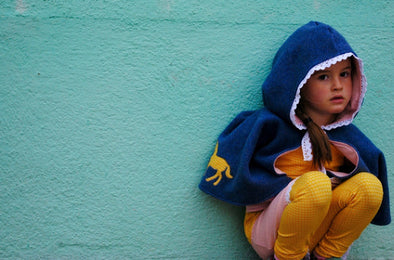 Mädchen in Cape aus Bio Baumwollfleece vor türkisem Hintergrund